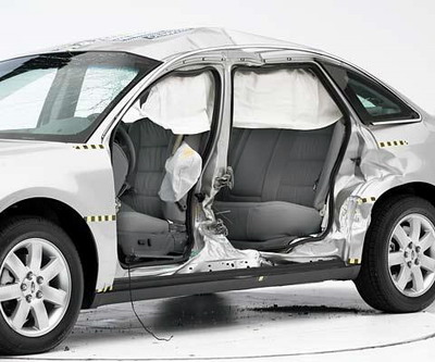 View of the vehicle after the crash with doors removed, showing the side airbags and damage to the occupant compartment.