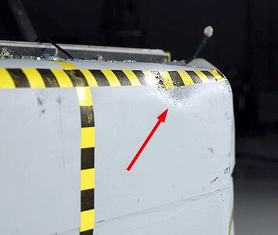 A prominent dent and embedded glass fragments indicate where the driver dummy's head hit the barrier